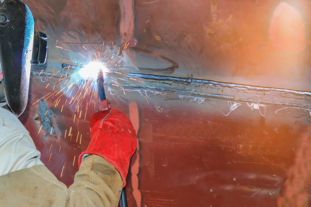 A Man Is Welding a Piece of Metal with A Welding Machine — Ashby Boat Builders In Buddina, QLD