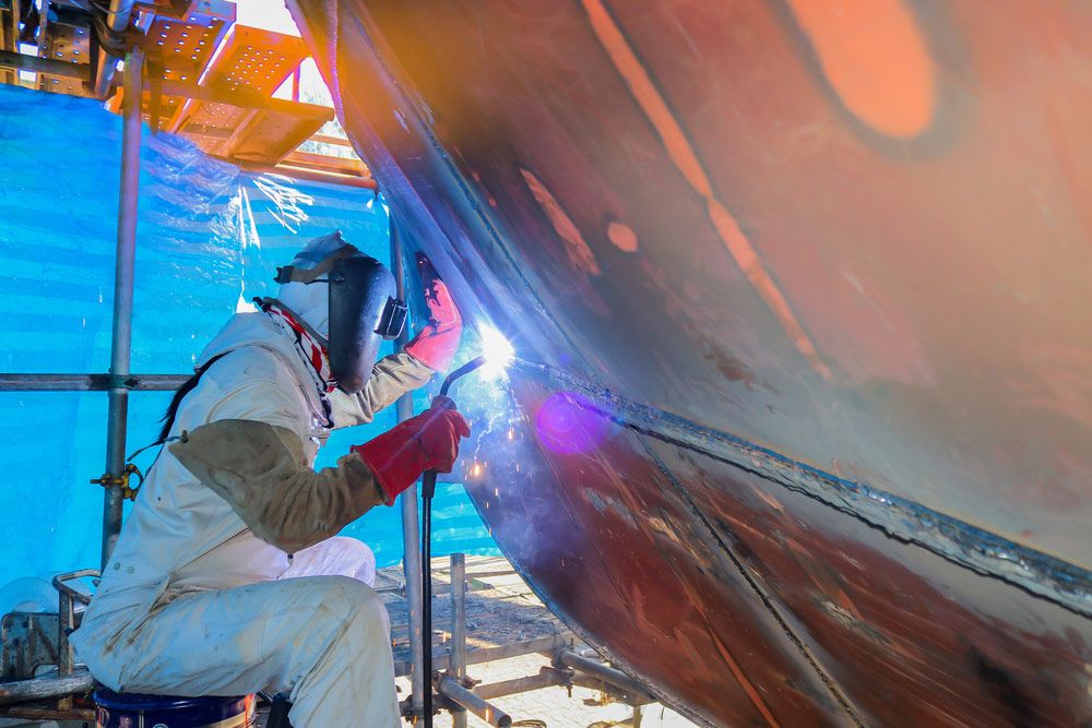 A Man Is Welding a Large Piece of Metal — Ashby Boat Builders In Buddina, QLD