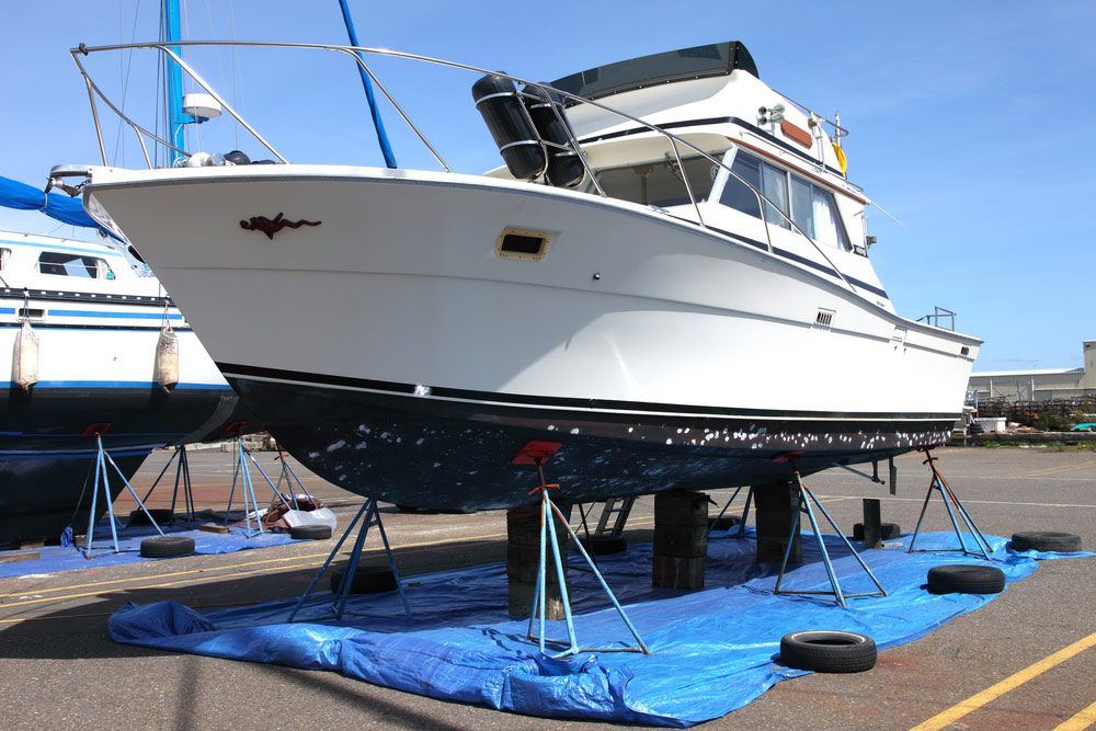 A Boat Is Sitting on A Blue Tarp in A Parking Lot — Ashby Boat Builders In Buddina, QLD