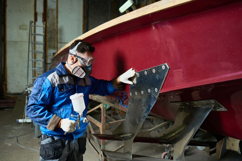 A Man Is Painting a Boat in A Warehouse — Ashby Boat Builders In Buddina, QLD