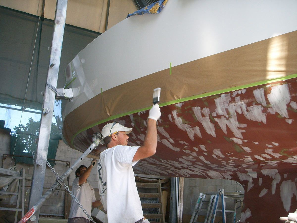A Man Is Painting a Boat with A Brush — Ashby Boat Builders In Buddina, QLD
