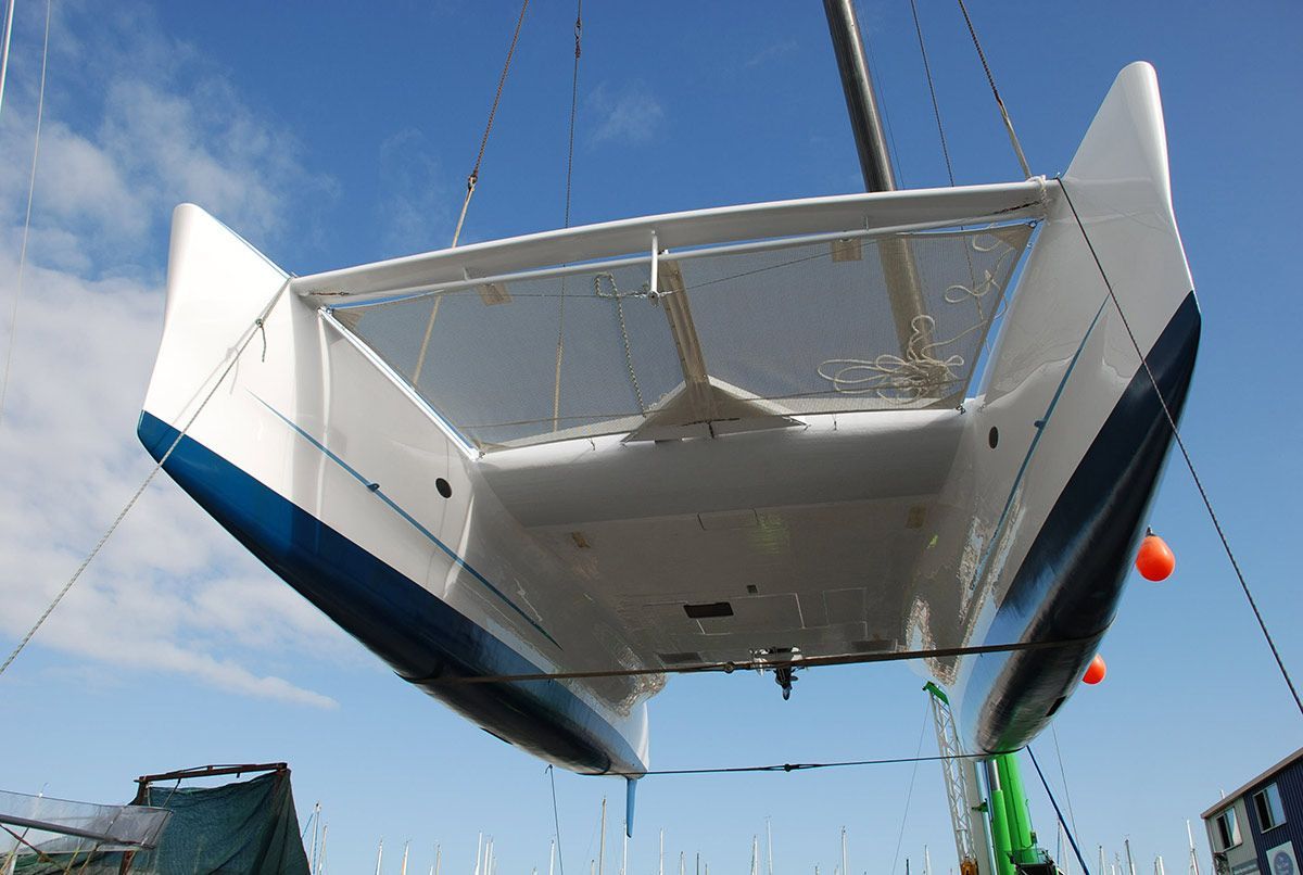 A White and Blue Sailboat Is Being Lifted by A Crane — Ashby Boat Builders In Buddina, QLD