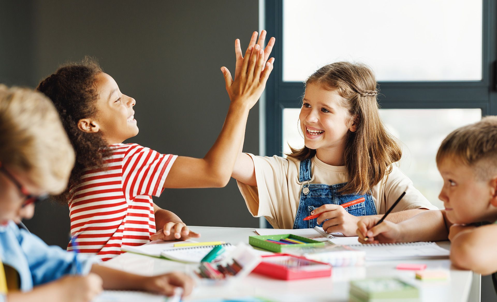 A group of children are sitting at a table giving each other a high five.