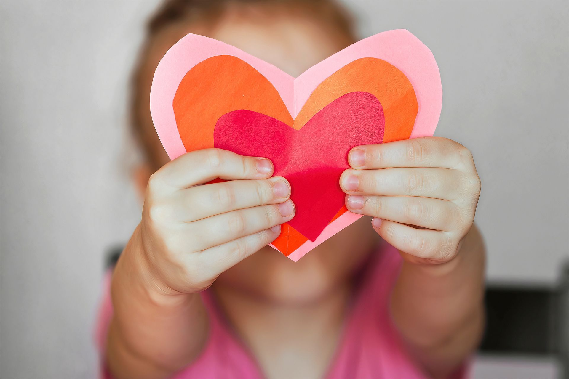 A little girl is holding a paper heart in front of her face.