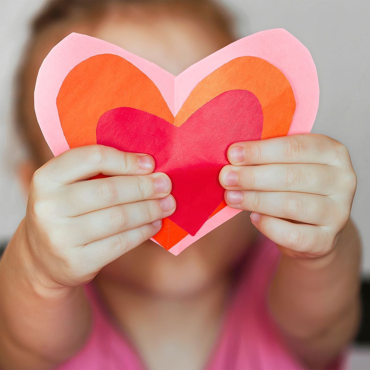 A little girl is holding a paper heart in front of her face