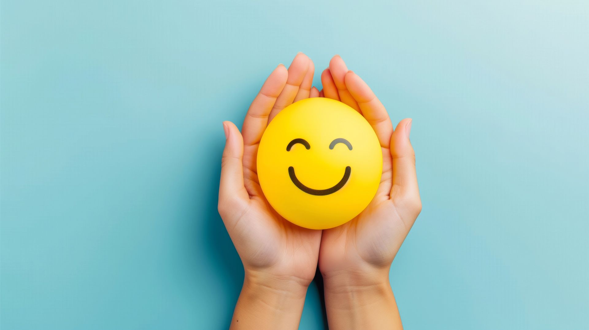 A person is holding a yellow smiley face in their hands.
