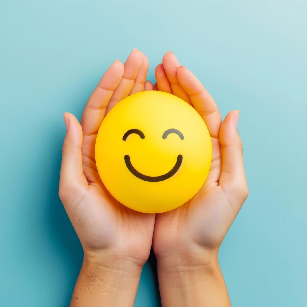 A person is holding a yellow smiley face in their hands.
