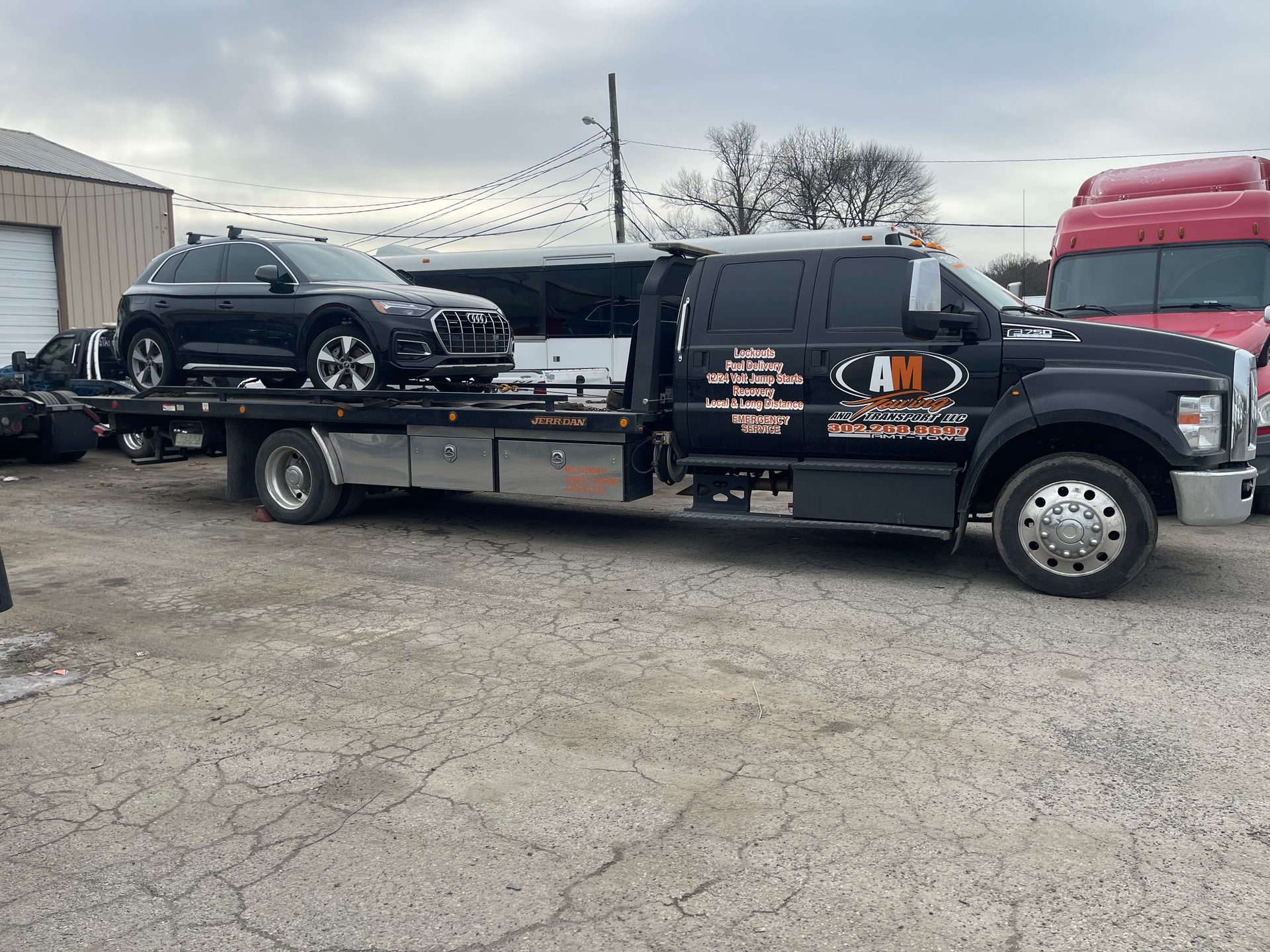 Black car on a flatbed tow truck; parked outdoors near a building, cloudy sky.
