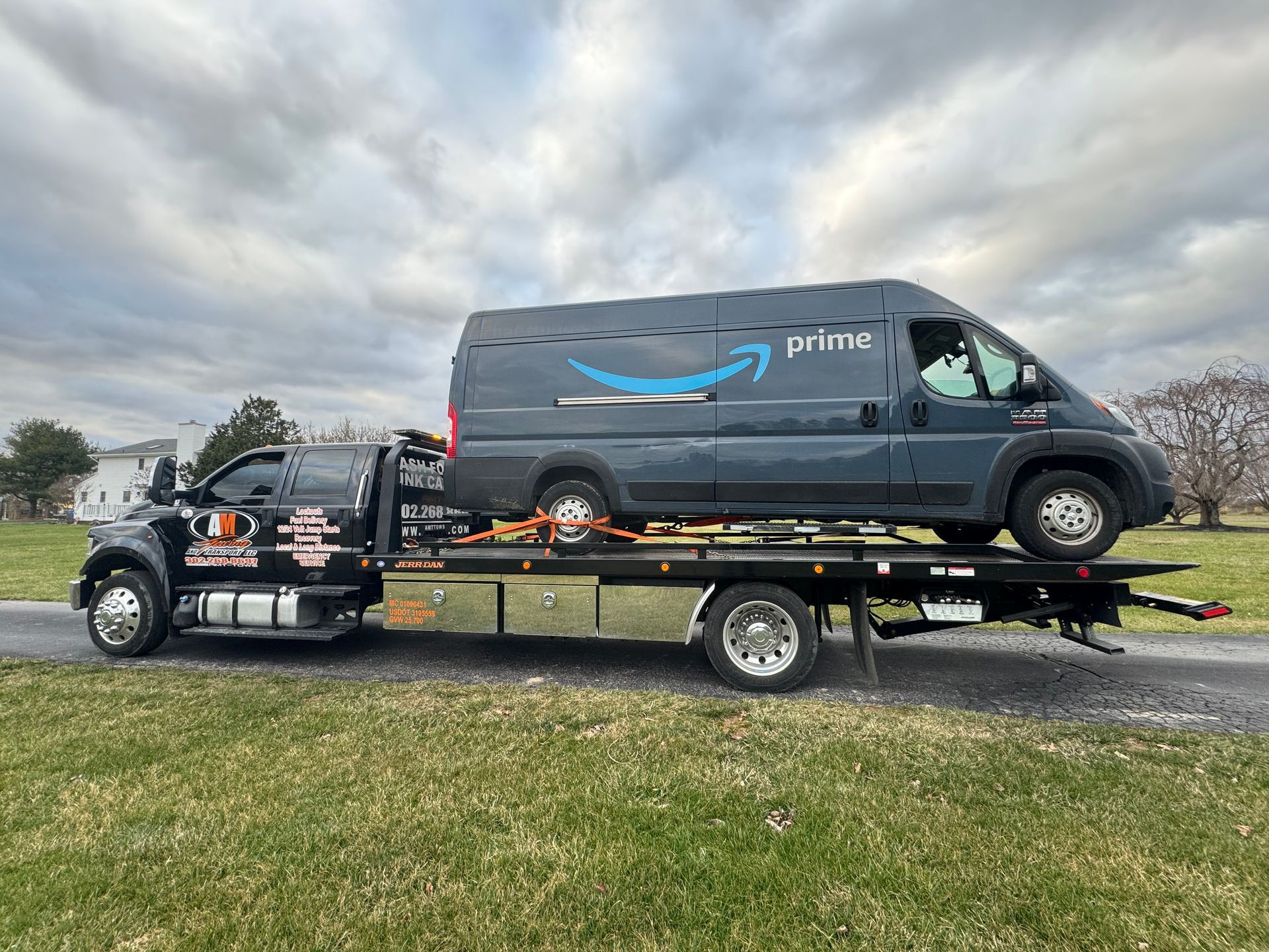 Tow truck carrying a gray Amazon Prime delivery van on a flatbed trailer, roadside.