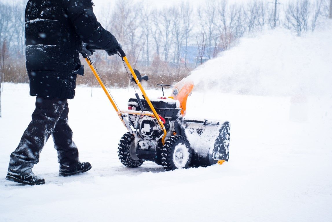 Person using a yellow snowblower to clear snow in a snowy outdoor area