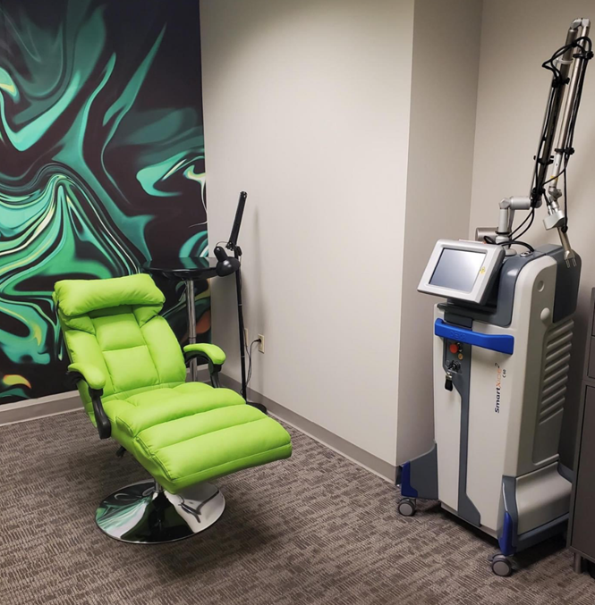 A medical room with a lime-green recliner, laser equipment, and abstract wall art.