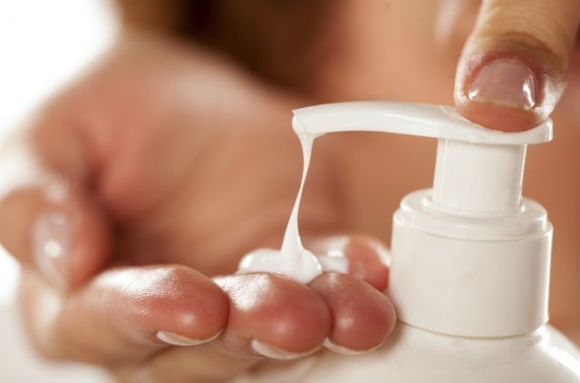 Hand dispensing white lotion from a white pump bottle.