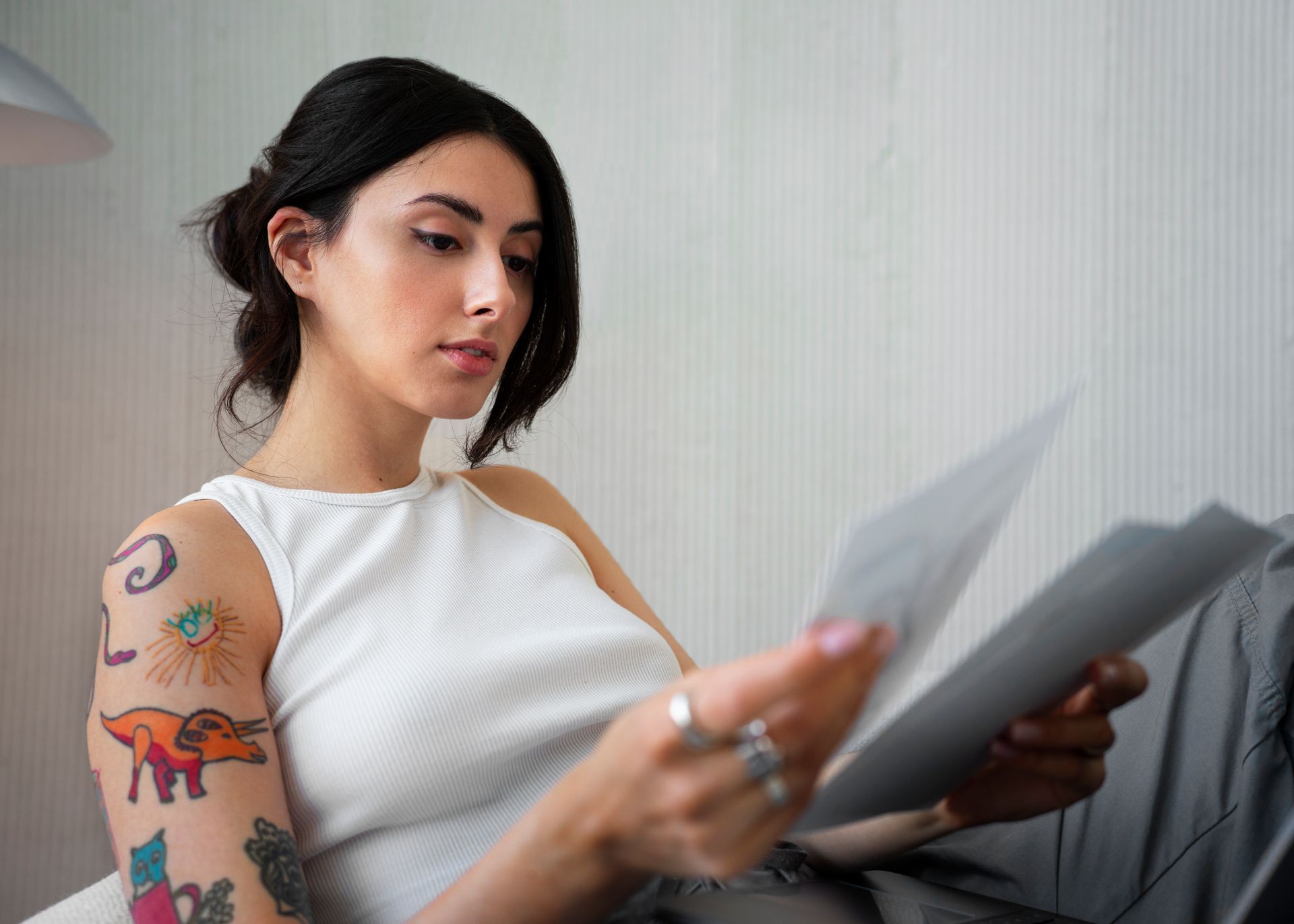 Woman with tattoos reads papers, seated indoors.