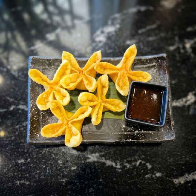 Fried flower-shaped pastries on a black plate with a small cup of dipping sauce