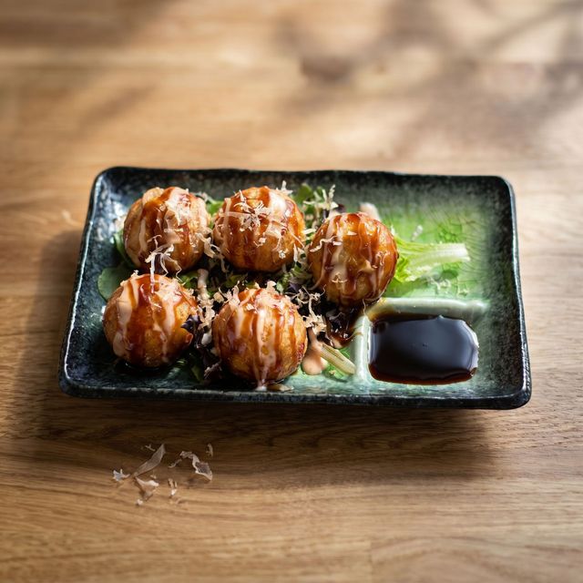 Five glazed meatballs on a black plate with greens and dark sauce on a wooden table
