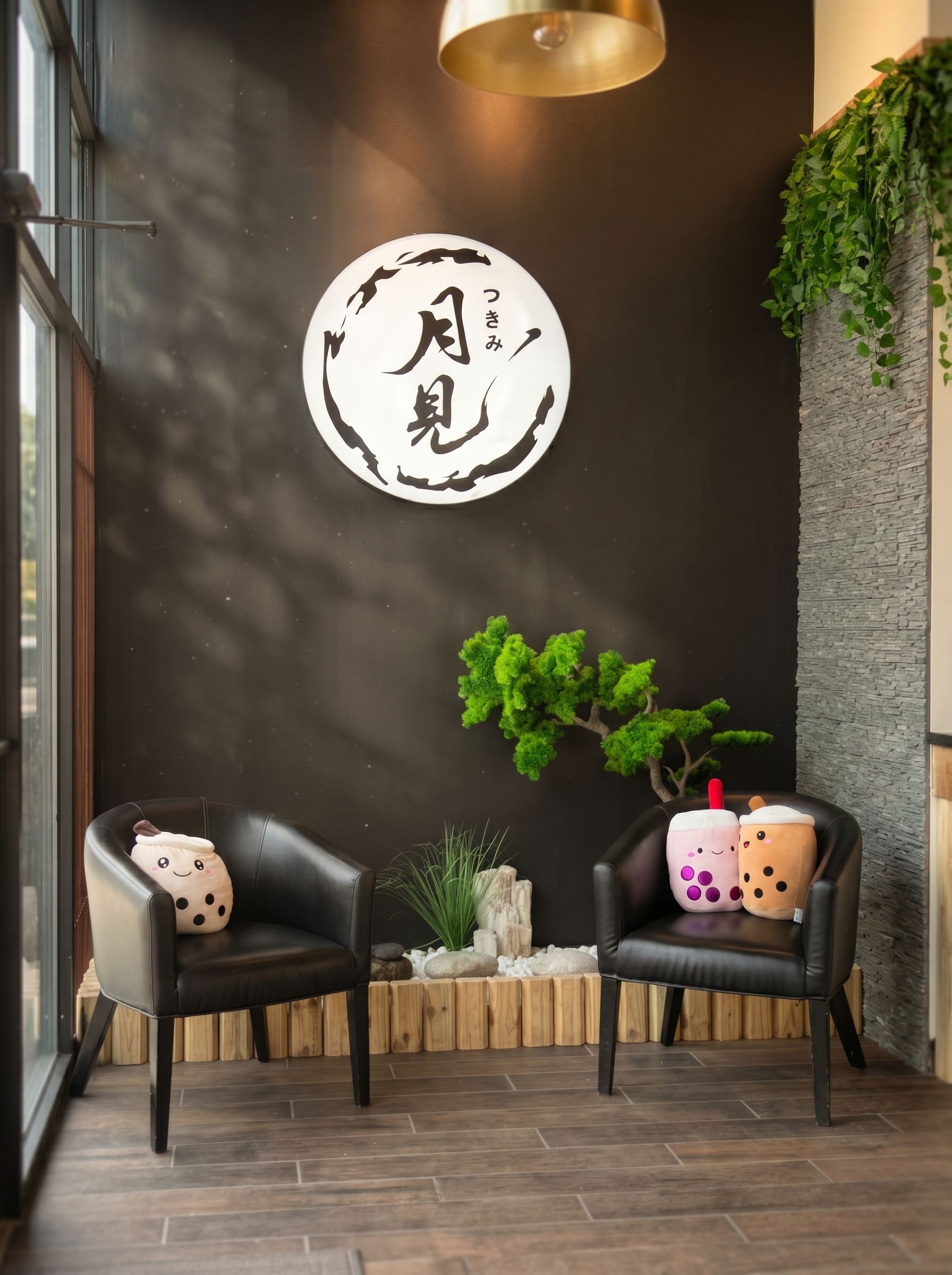 Modern lounge with two black chairs, small table, hanging plant, and circular wall sign on a dark wall.