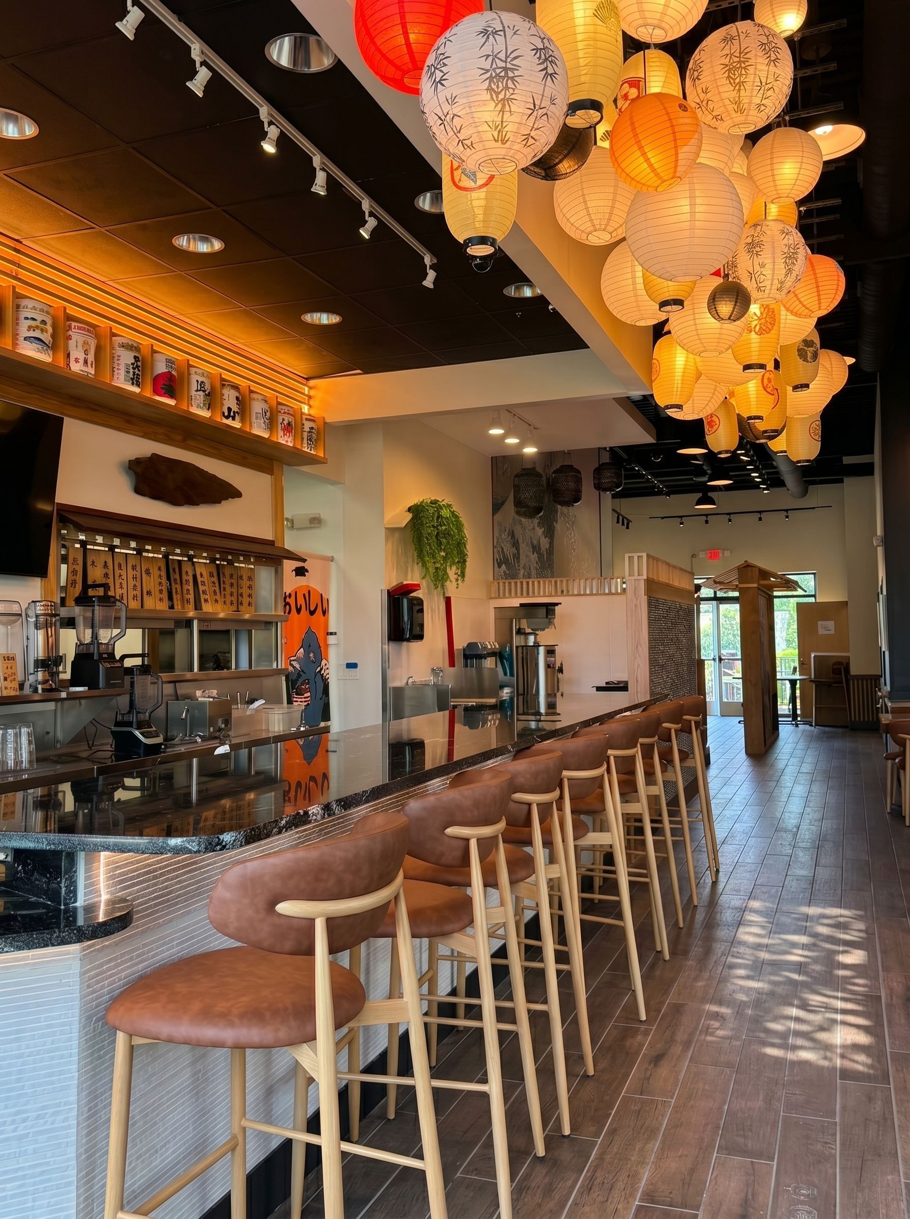 Cozy bar interior with wooden stools, warm hanging lanterns, and a long counter along the left wall.