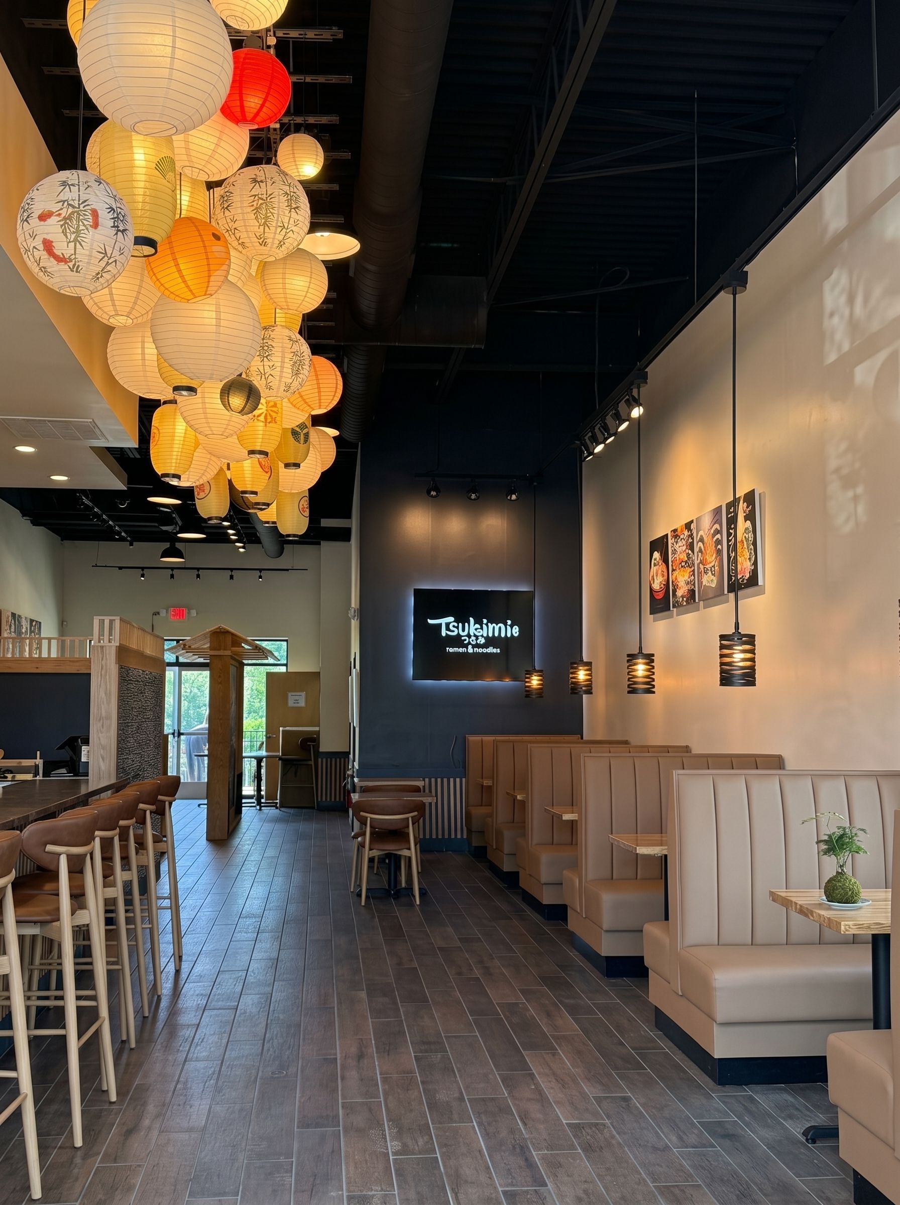 Modern café interior with hanging lanterns, wood floors, bar stools, and booth seating