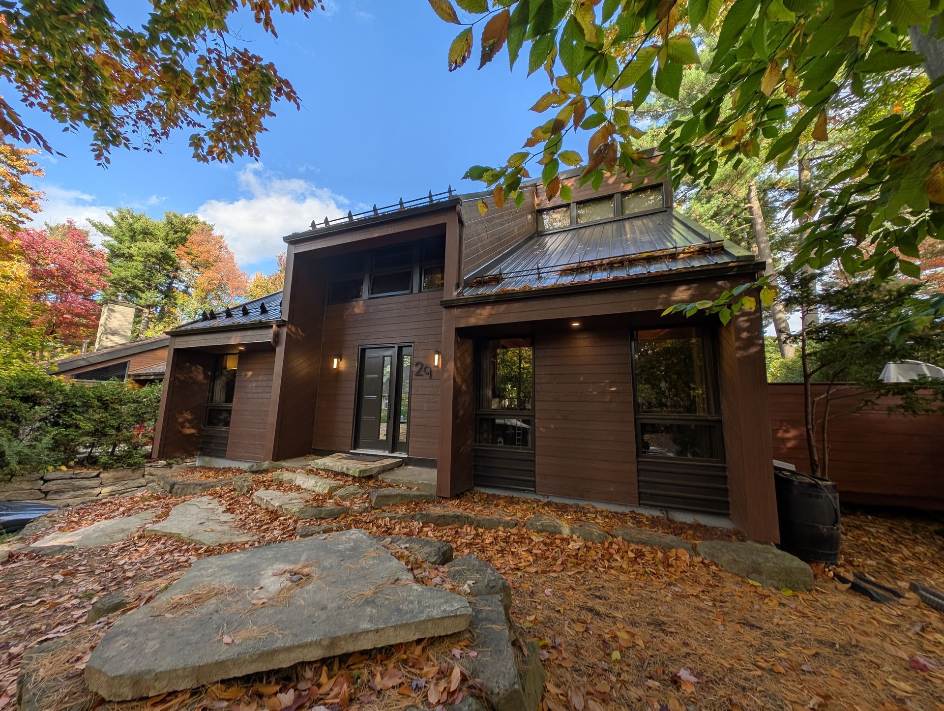 Maison rustique brune avec des feuilles d'automne et un gros rocher au premier plan sous un ciel bleu