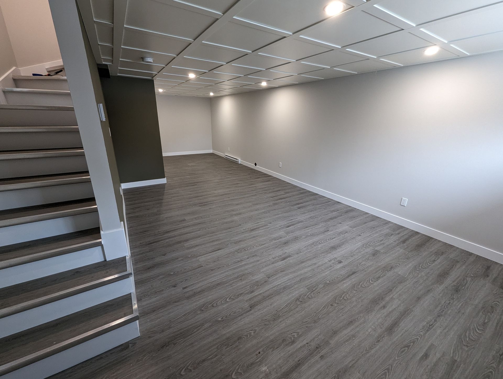 Un sous-sol vide avec parquet et escaliers en bois.