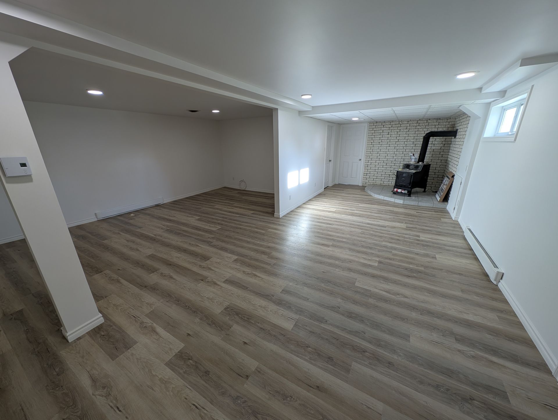Pièce rénovée vide avec parquet, murs blancs, éclairage encastré et coin cheminée en marbre