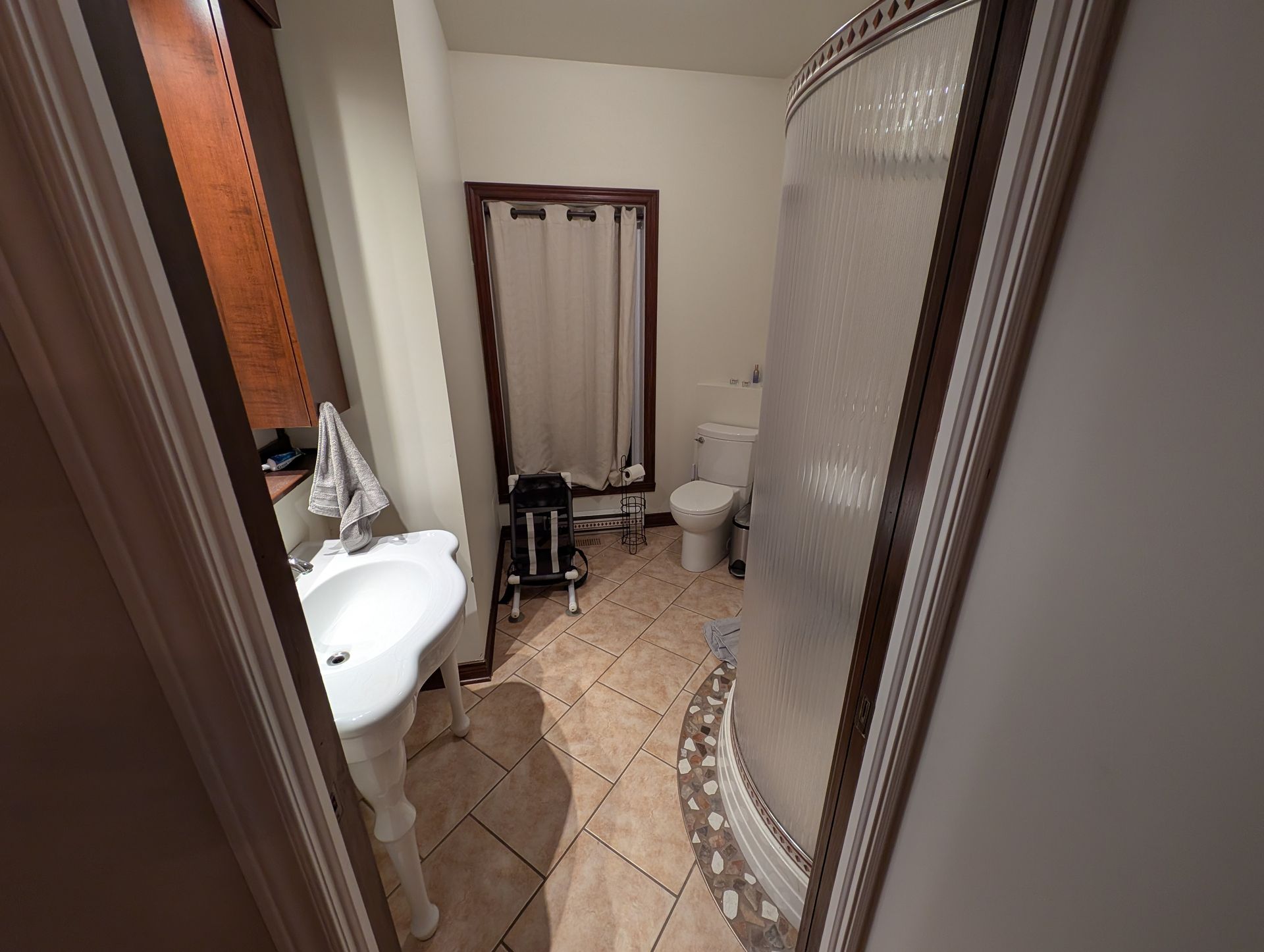 Salle de bain étroite avec lavabo, toilettes, douche et un déambulateur près du rideau de douche.