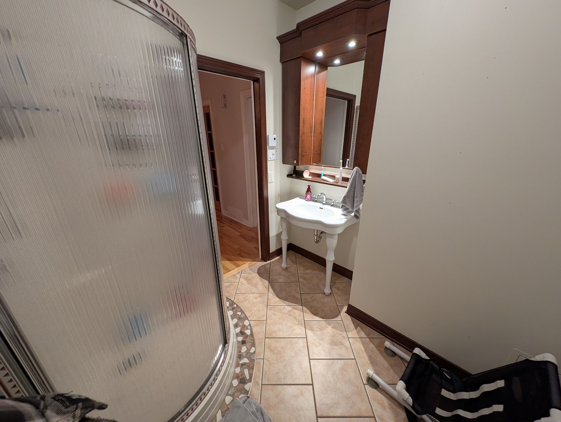 Salle de bains avec douche, lavabo et sol carrelé ; un tabouret noir est placé près du mur.
