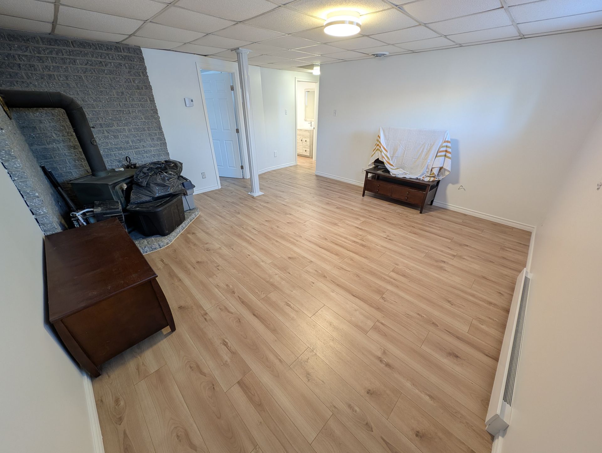 Salon vide avec parquet clair, murs blancs, cheminée et petite table près de la fenêtre.