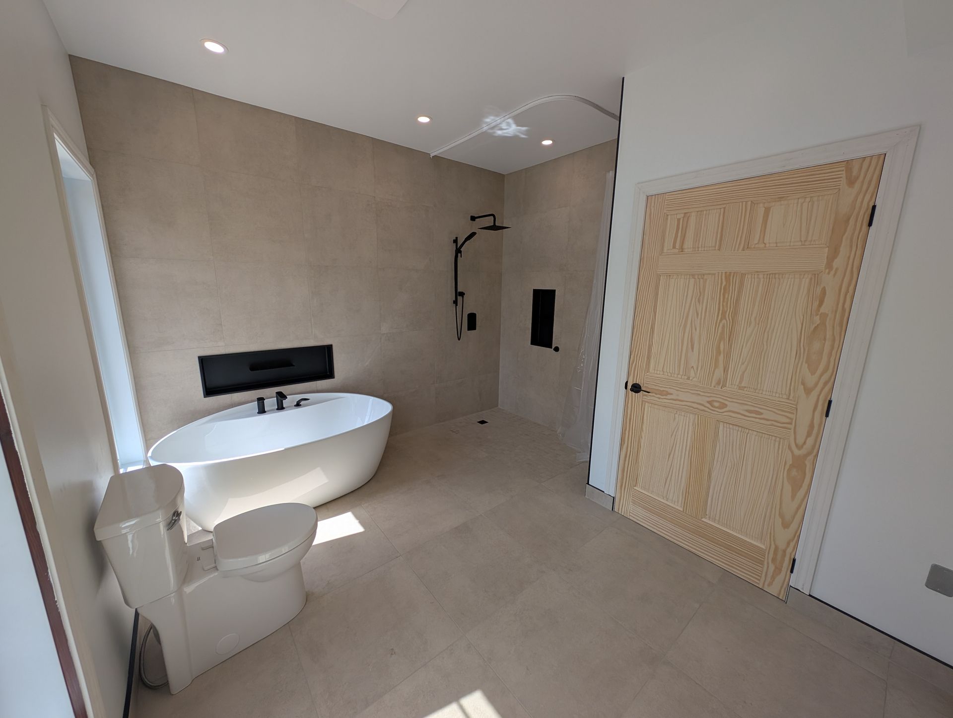 Salle de bains moderne beige avec baignoire îlot, douche à l'italienne, toilettes et portes doubles en bois