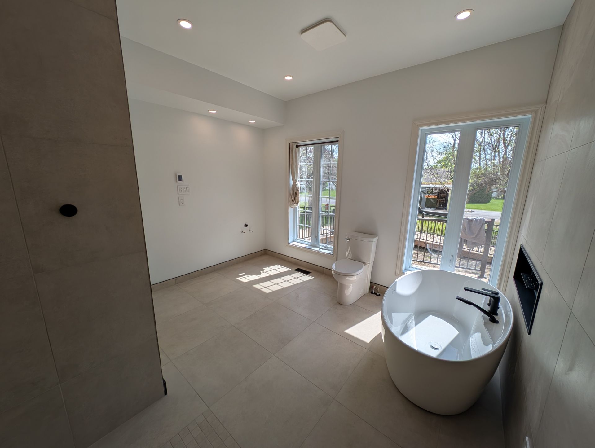 Salle de bains moderne avec toilettes, baignoire îlot, portes vitrées et sol carrelé clair.