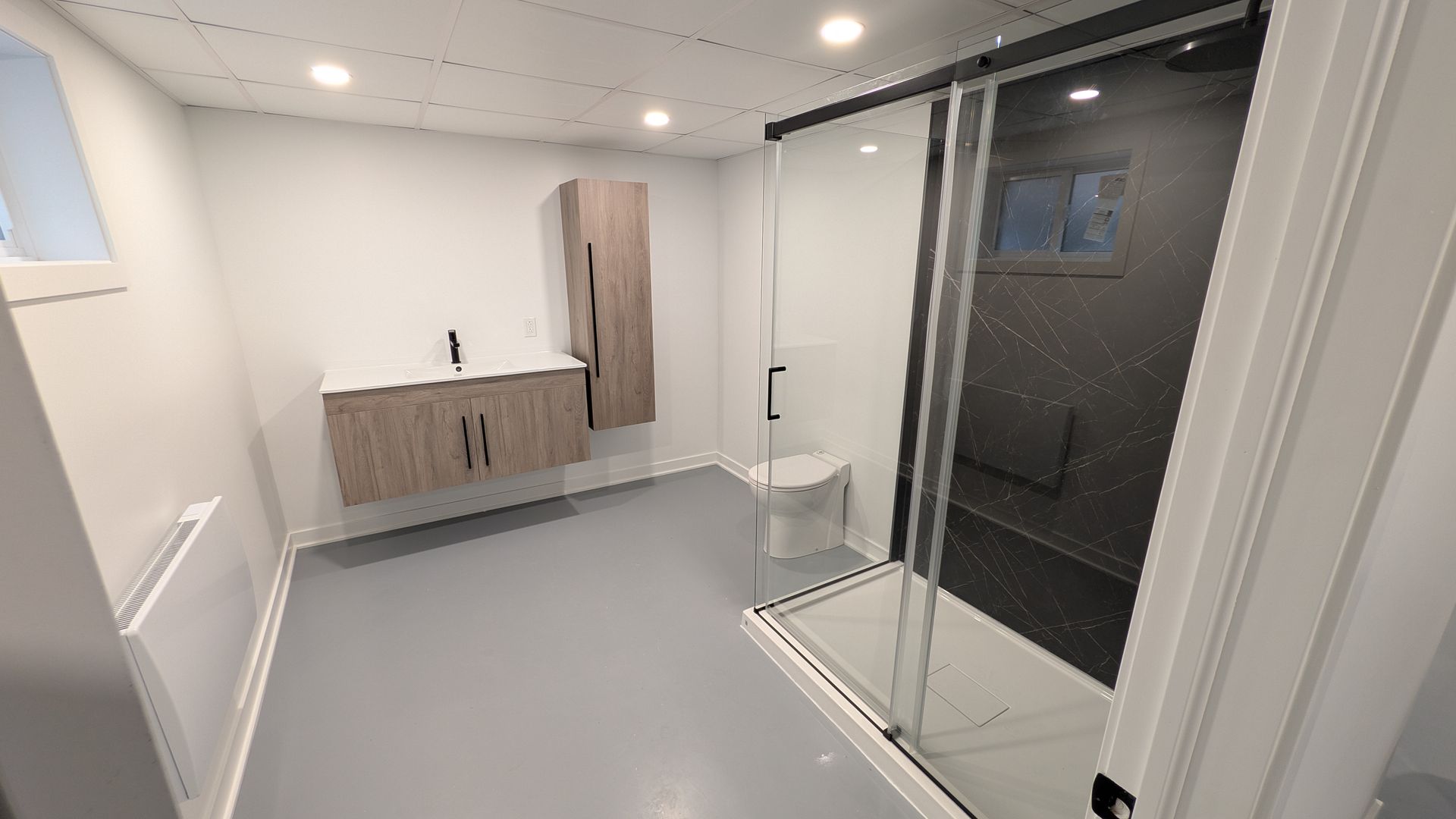 Salle de bains moderne avec meuble-lavabo, toilettes, douche en verre et sol gris clair