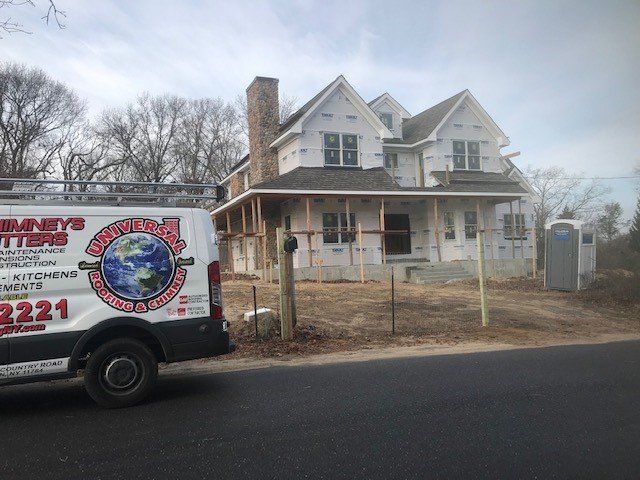 House under construction; scaffolding, covered in wrap; stone chimney; portable toilet; work van.