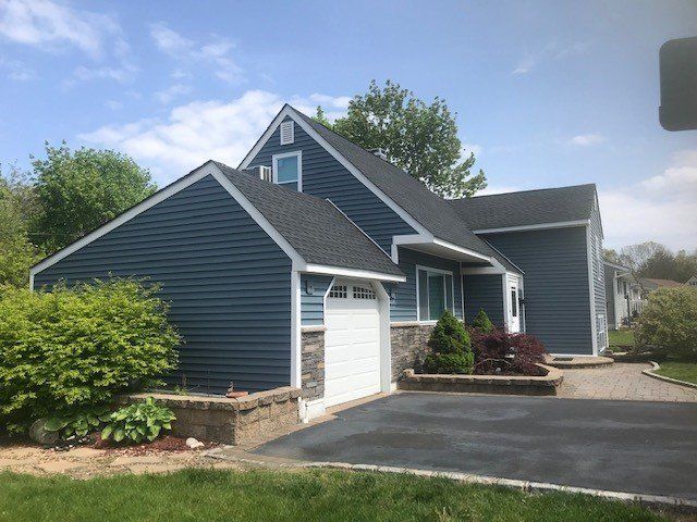 Blue-sided house with a dark roof and white garage door. Brickwork and driveway in front.