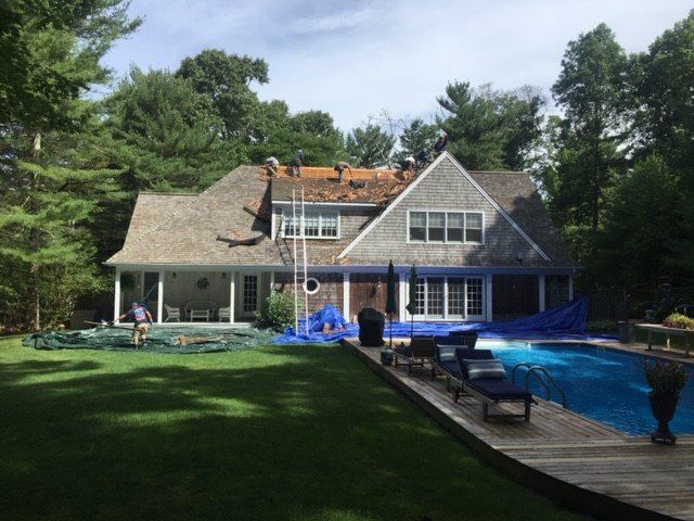 Roofers working on a house with a pool, covered in blue tarp, on a sunny day.