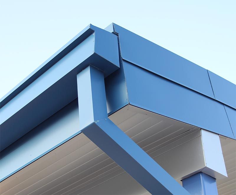 Blue building corner with gutter and downspout against a pale blue sky.
