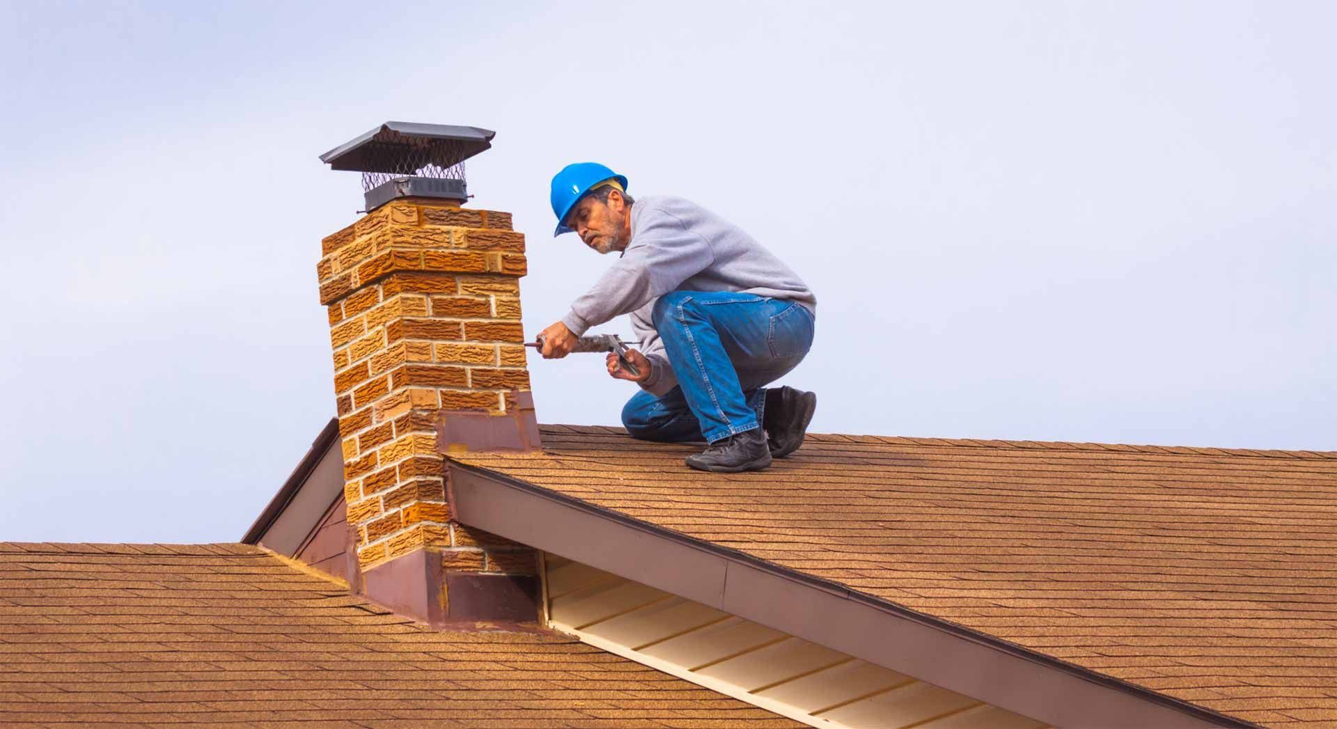 Chimney repairman on a brown shingled roof, examining the brick chimney with a metal cap.
