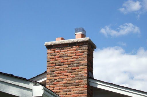 Brick chimney with a stainless steel cap against a blue sky with clouds.