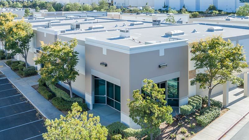 Industrial building exterior with beige walls, glass doors, and trees.