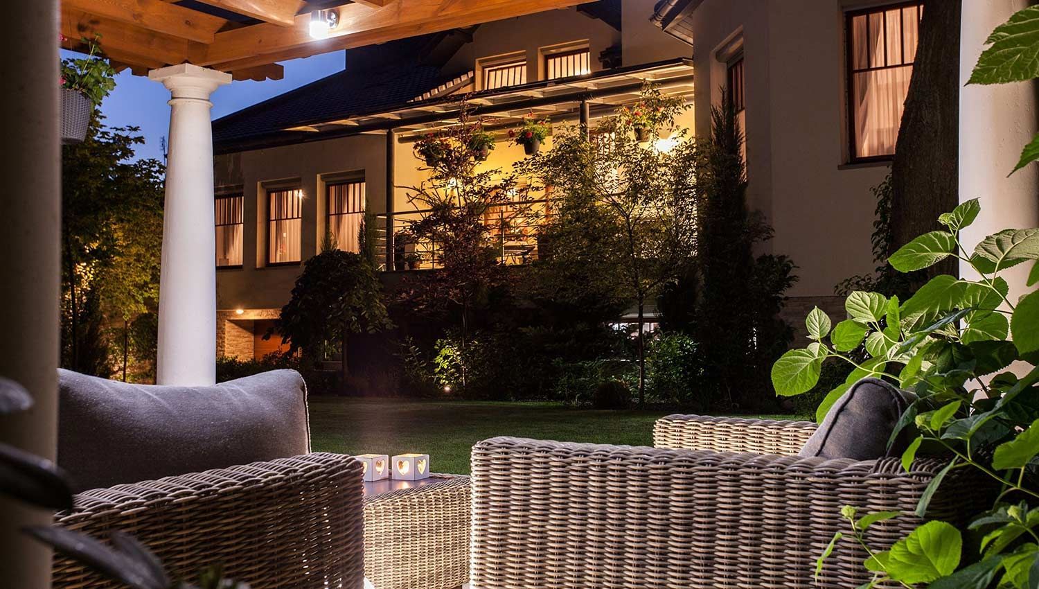 Cozy outdoor seating area at night with wicker furniture and a lighted patio, overlooking a building with lit windows.