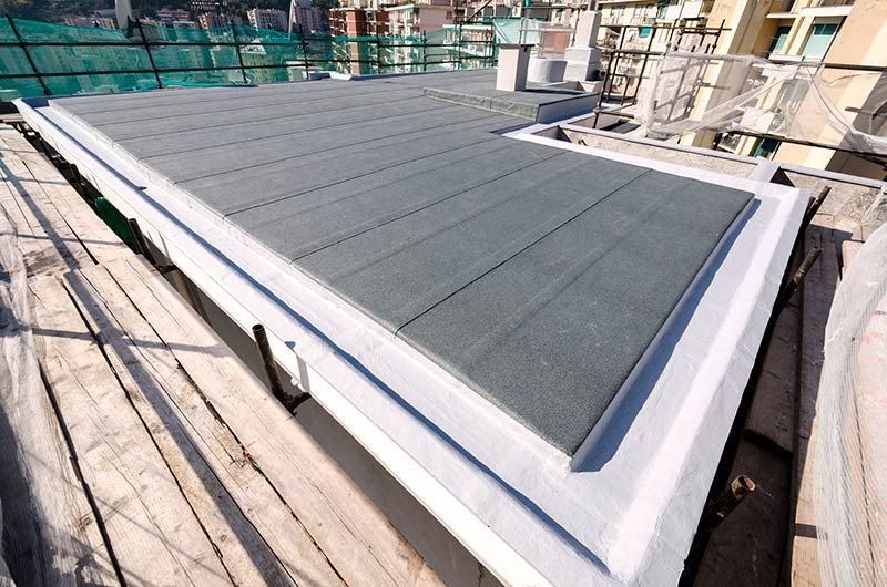 Flat roof with gray surface, white trim, and cityscape background.
