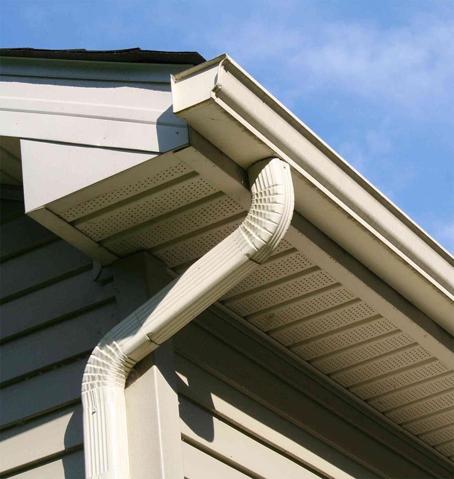 Beige house exterior with white gutters and downspout against a blue sky.