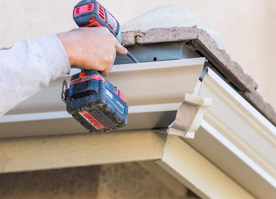 Person using a drill to install a gutter on a building's roof.