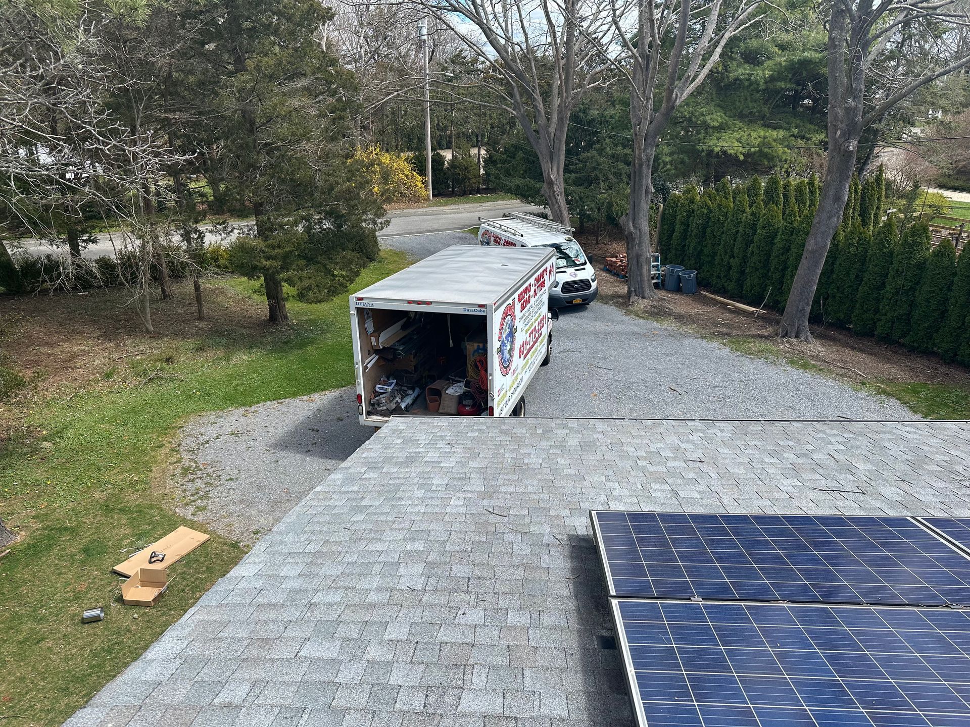 A moving truck parked on a gravel driveway next to a house with solar panels on the roof.