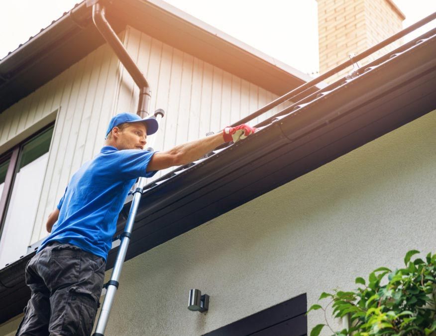 Man on ladder cleaning gutters of a house.