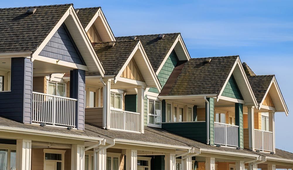 Row of colorful houses with gabled roofs, balconies, and white trim against a blue sky.