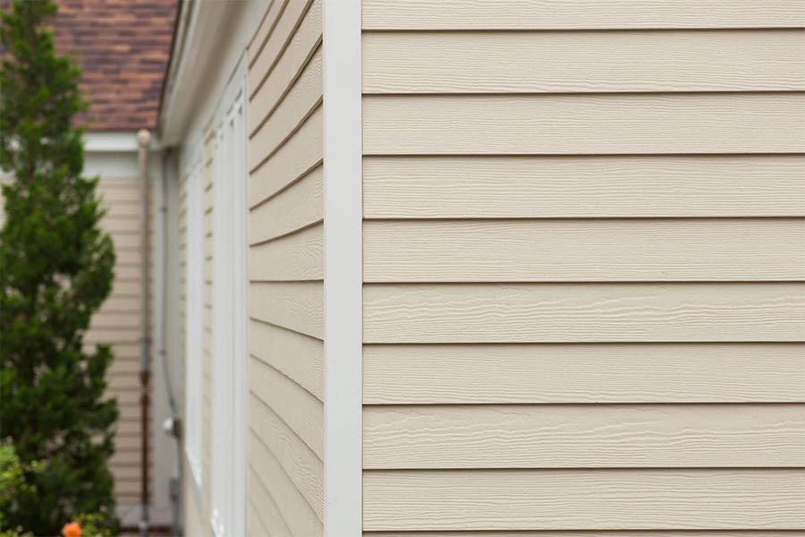 Beige siding on a house exterior with white trim around windows.