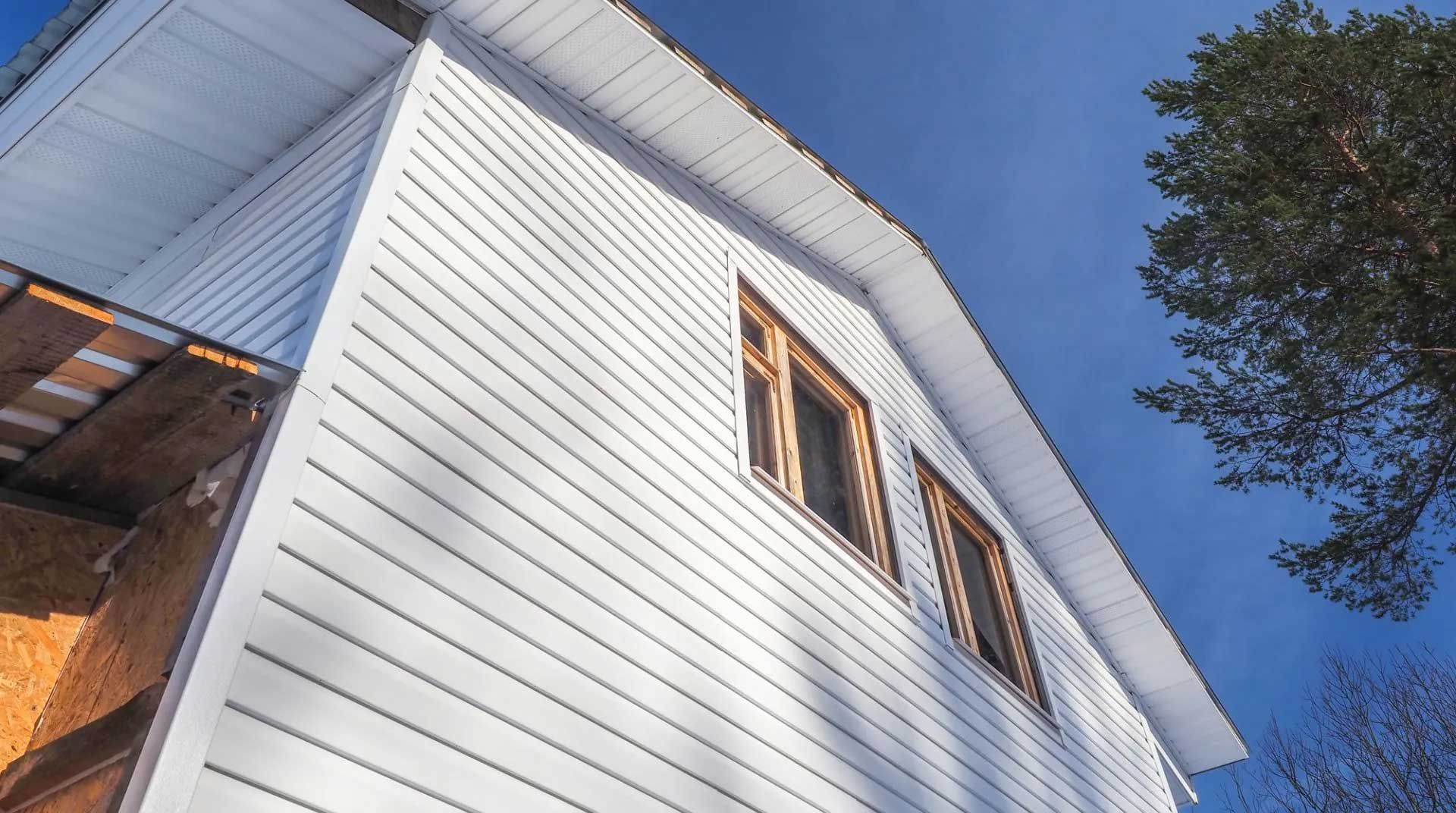 White-sided house with wooden-framed windows against a bright blue sky.