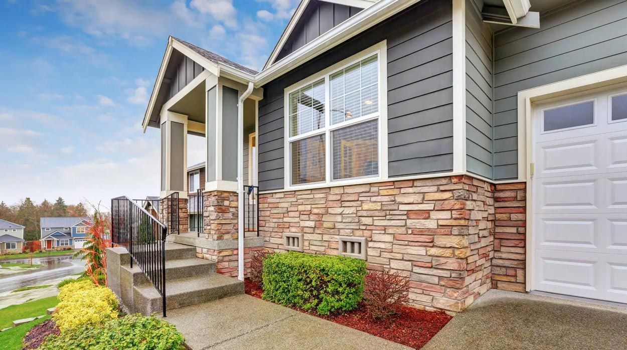 House exterior with gray siding, stone facade, and a white garage door.