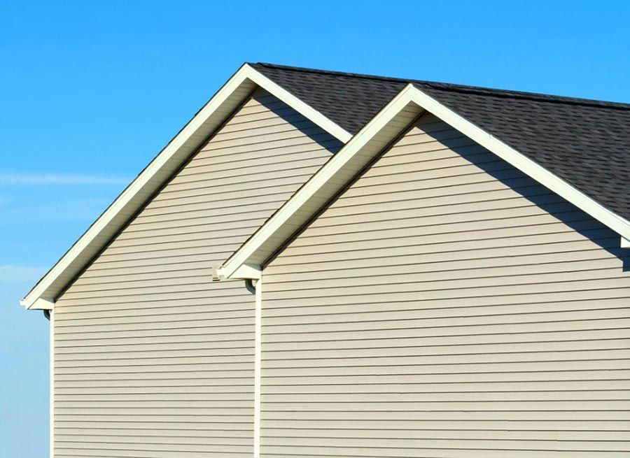 Two-story house with light siding and dark roof against a clear blue sky.