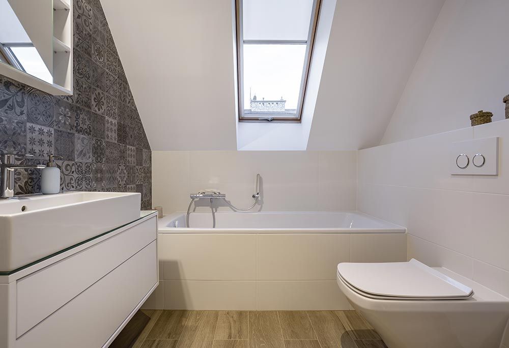 Bathroom with a white bathtub, toilet, and sink. Patterned wall tile and a skylight.